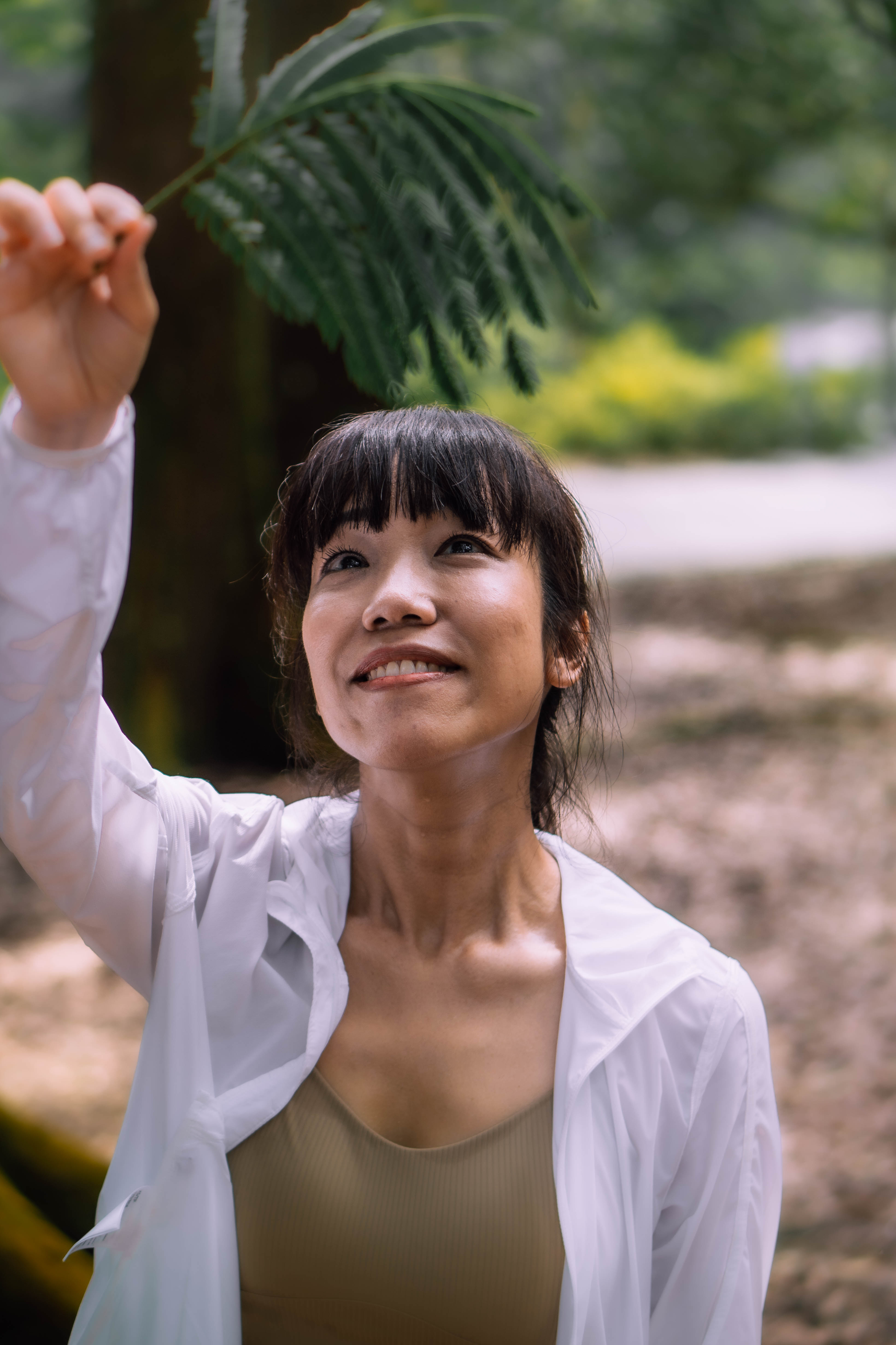 Hazel Yap looking up at the forest canopy, holding a leaf